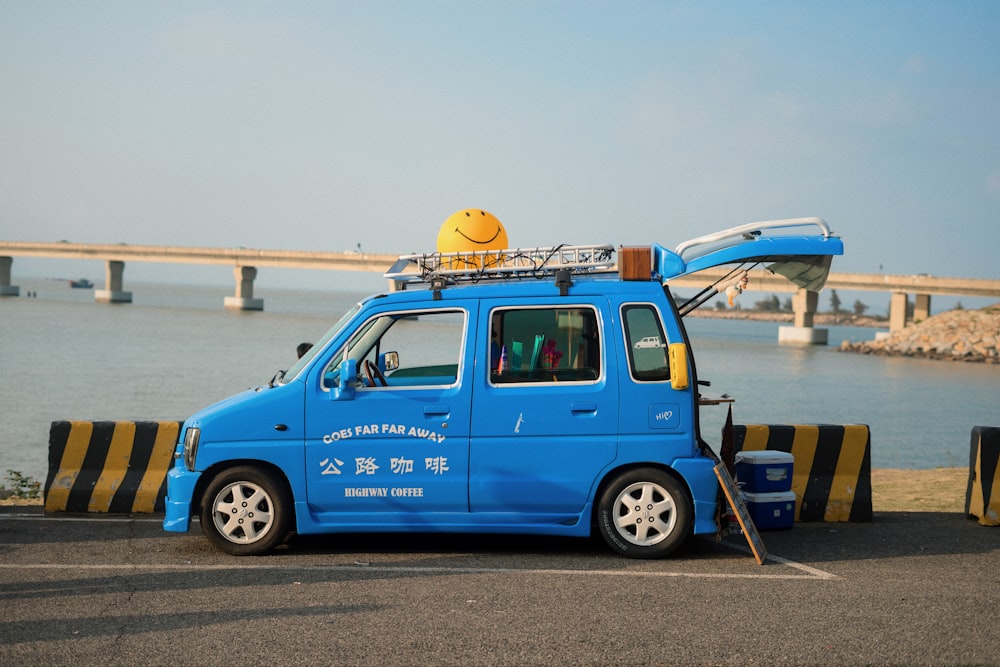 a small blue van parked in a parking lot next to a body of water