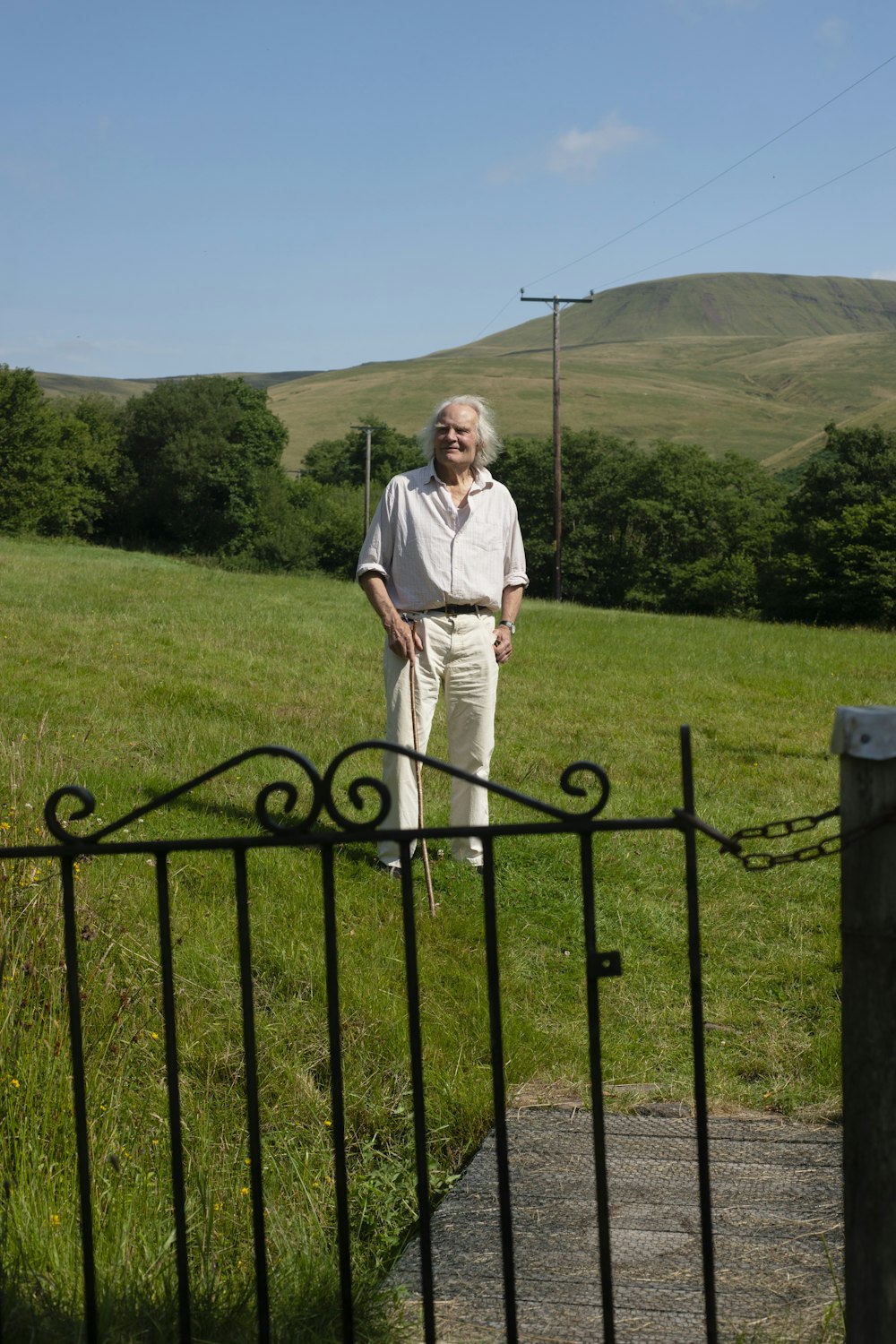 an old man standing in the grass near a fence