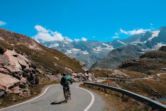 A biker riding along a winding road with mountains in the background under a clear blue sky.