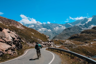 A cyclist riding along a winding mountain road with panoramic Himalayan views.