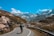 A cyclist riding through a scenic mountain landscape with lush greenery and distant peaks.