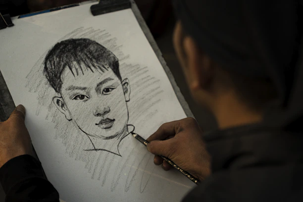 An artist's hand sketching a detailed portrait on textured paper.