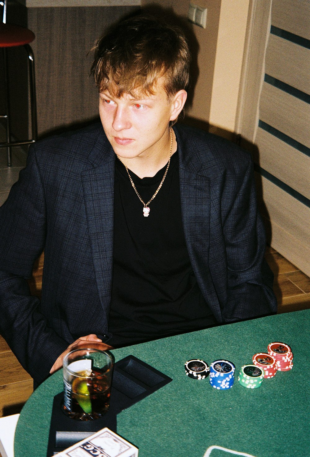 a man sitting at a table with a drink and playing cards