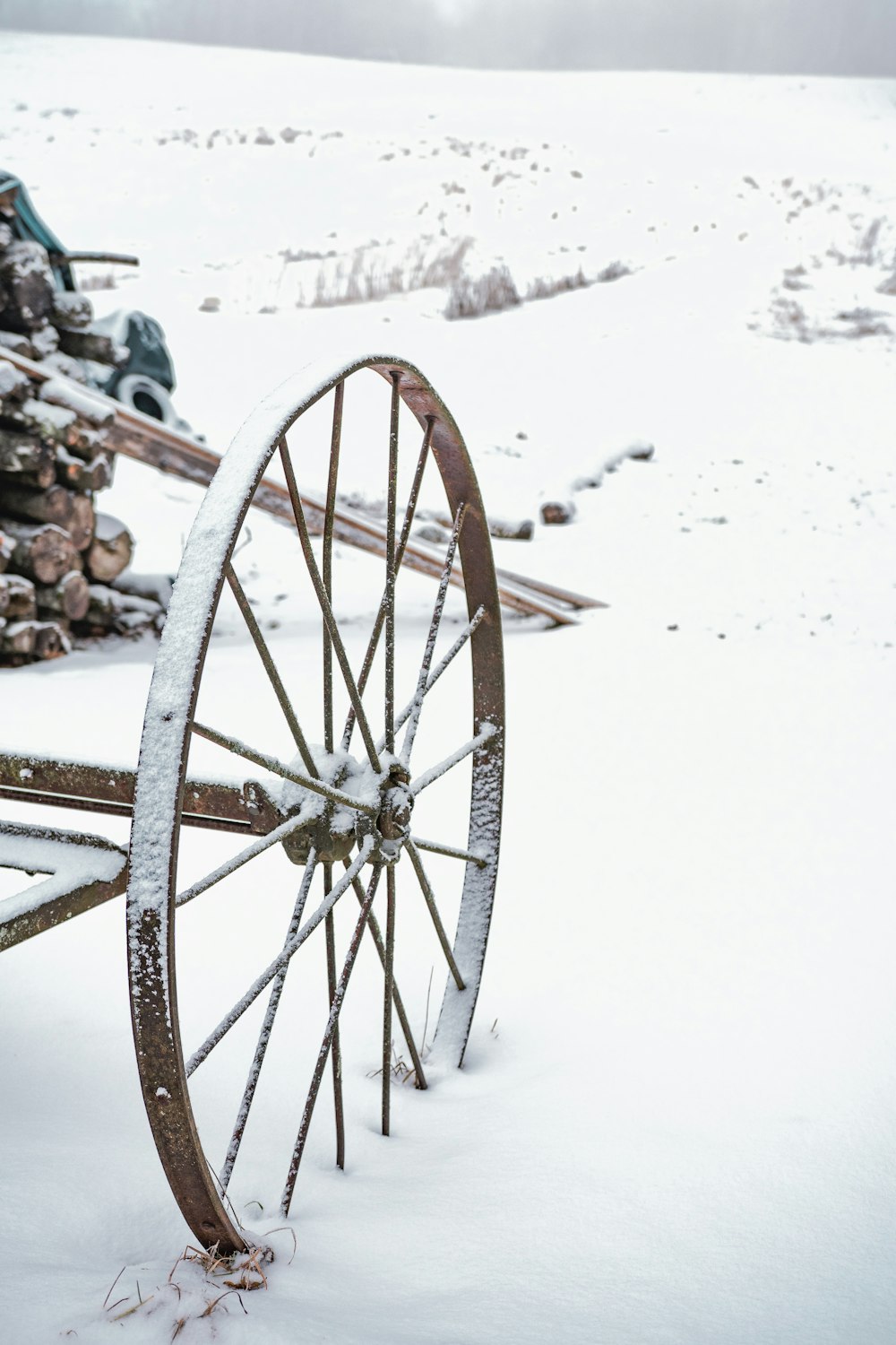 an old wagon is covered in snow in front of a pile of logs