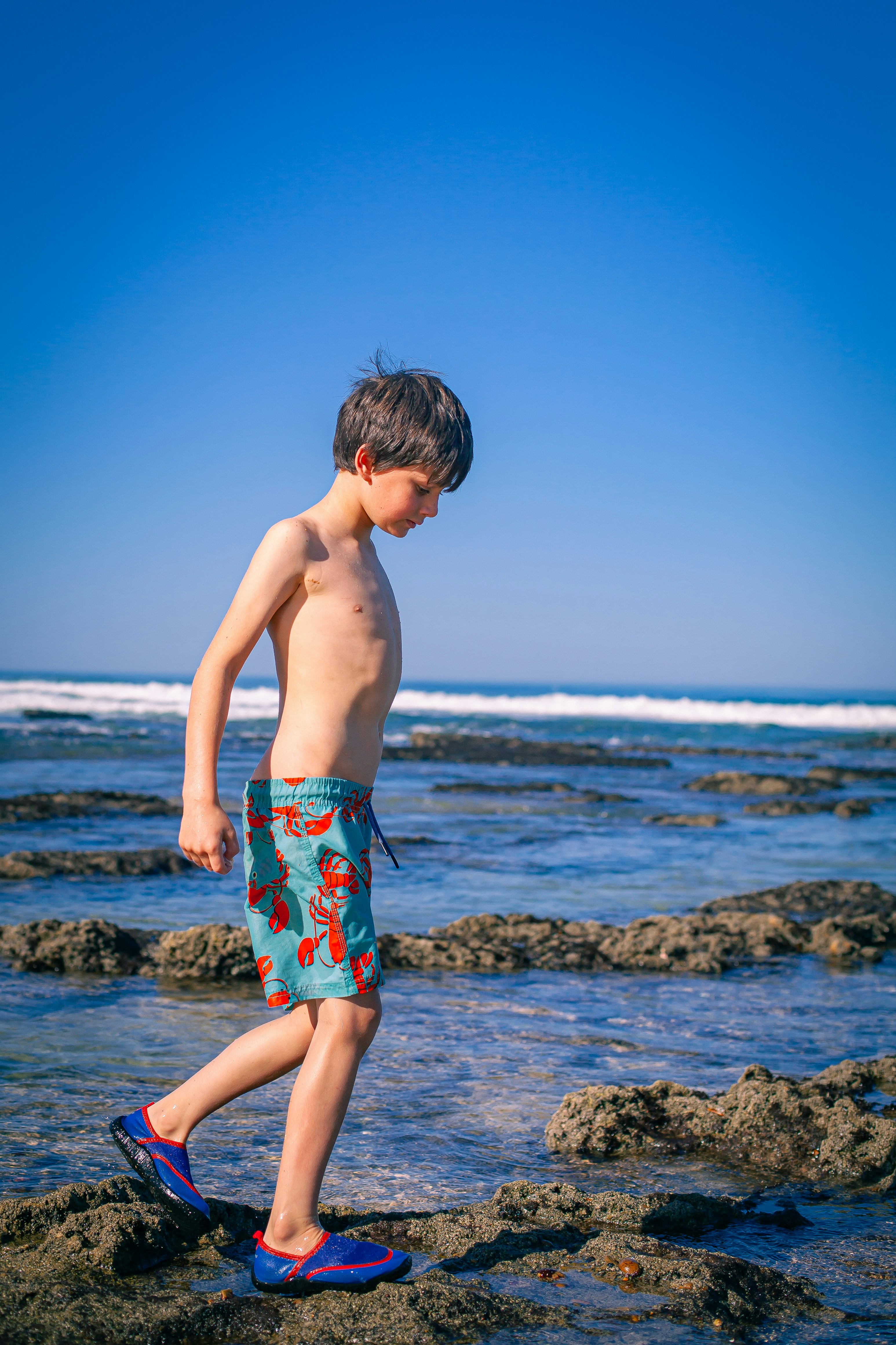 a young boy standing on top of a rock covered beach