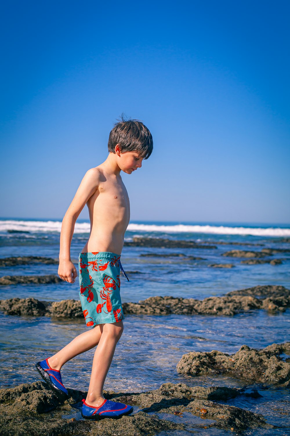 a young boy standing on top of a rock covered beach