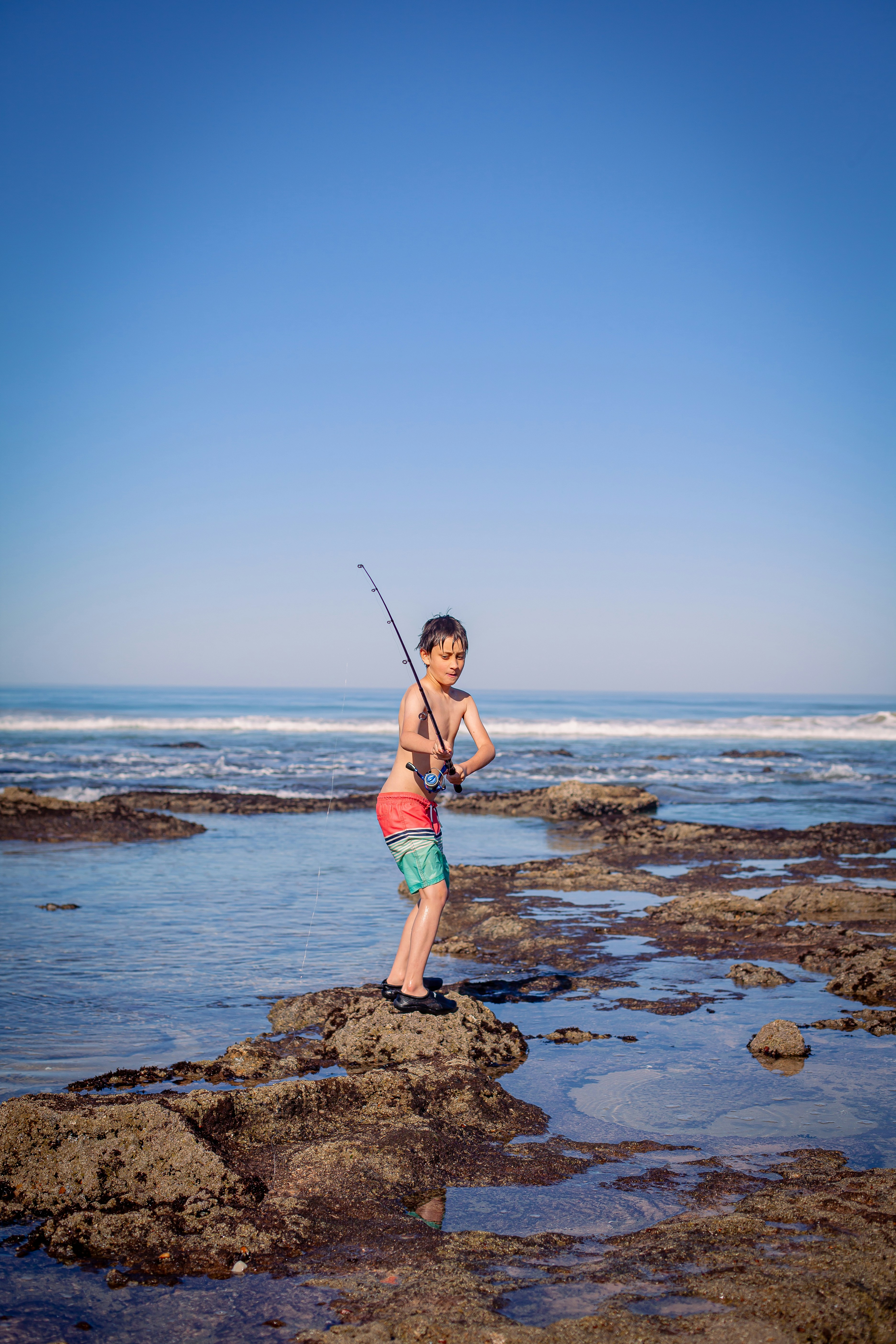 a young boy holding a fishing rod on a rocky beach