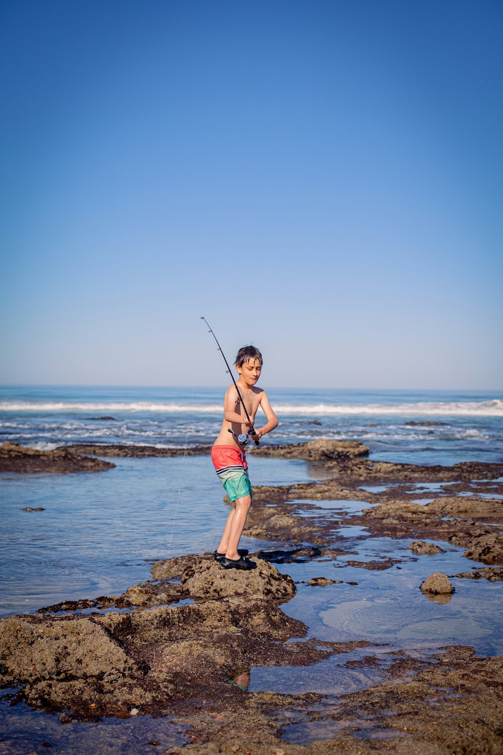 a young boy holding a fishing rod on a rocky beach