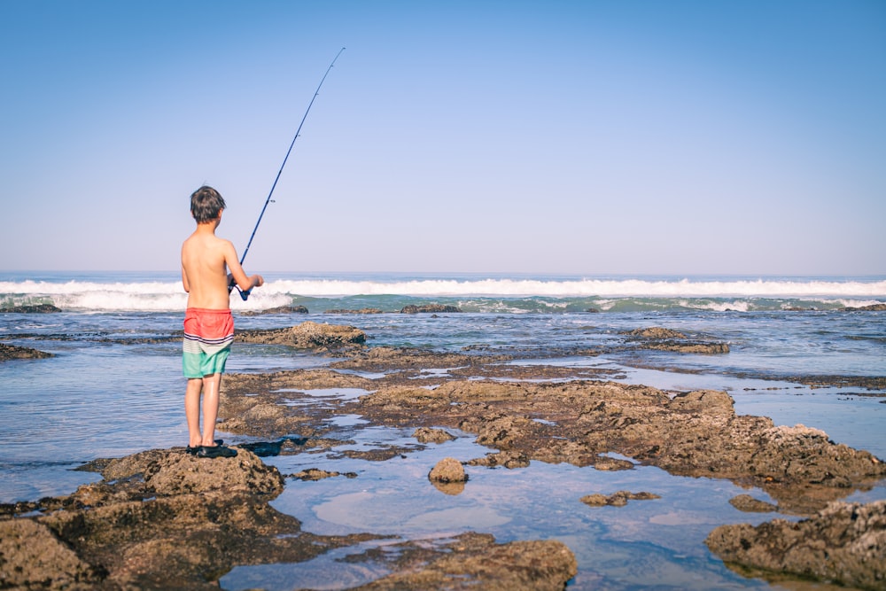 a man standing on top of a rocky beach holding a fishing pole