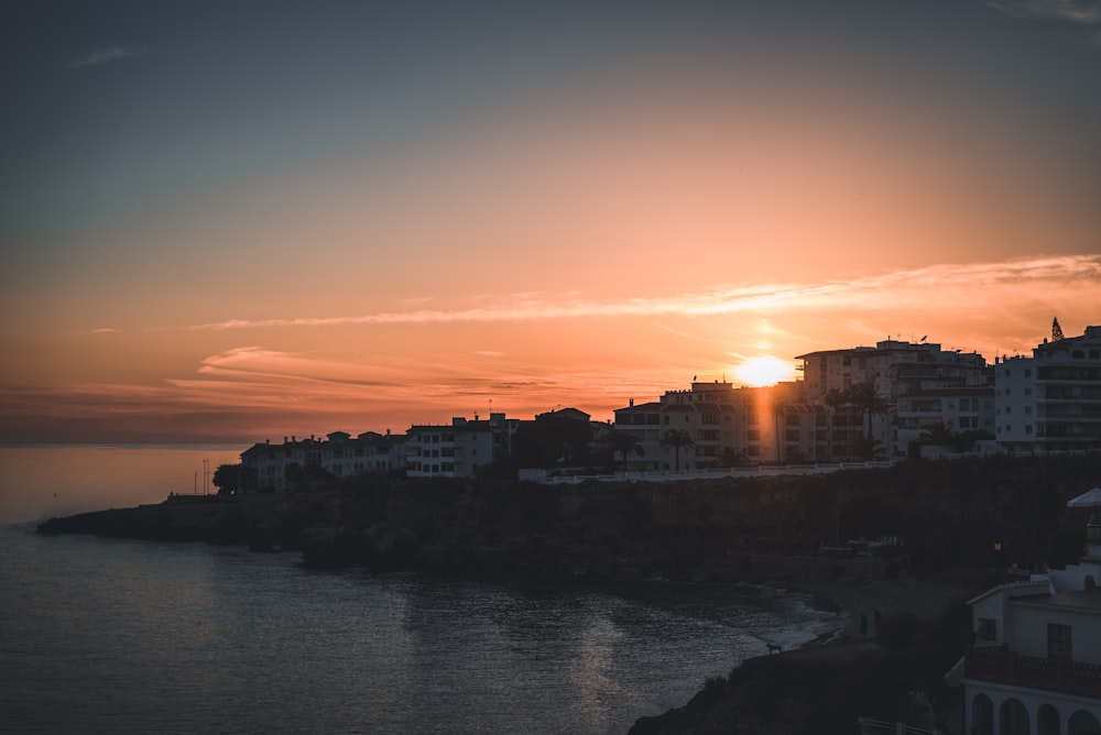 the sun is setting over a city by the water