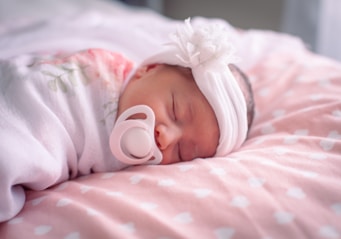 a baby with a pacifier laying on a pink blanket