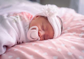 a baby with a pacifier laying on a pink blanket