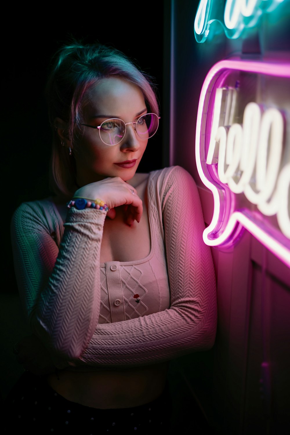 a woman wearing glasses standing in front of a neon sign