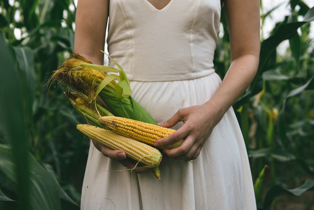 a woman in a white dress holding a corn cob