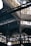 An intricate metal framework supports a large industrial ceiling. The structure includes various beams and ornate designs with light filtering through slotted windows. The scene is reminiscent of an old factory or market hall with its heavy reliance on metal construction.