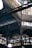 An intricate metal framework supports a large industrial ceiling. The structure includes various beams and ornate designs with light filtering through slotted windows. The scene is reminiscent of an old factory or market hall with its heavy reliance on metal construction.