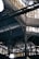 An intricate metal framework supports a large industrial ceiling. The structure includes various beams and ornate designs with light filtering through slotted windows. The scene is reminiscent of an old factory or market hall with its heavy reliance on metal construction.