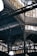 An intricate metal framework supports a large industrial ceiling. The structure includes various beams and ornate designs with light filtering through slotted windows. The scene is reminiscent of an old factory or market hall with its heavy reliance on metal construction.