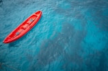 Close-up of a bright red kayak gliding through crystal-clear water near rocky shores