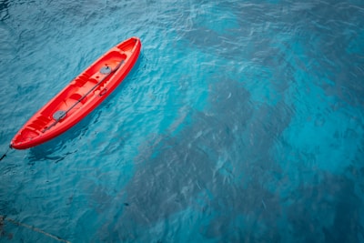 Close-up of a bright red kayak gliding through crystal-clear water near rocky shores
