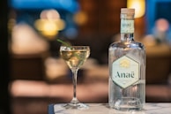 A serene evening setting with barbesini.gin bottle and glass on a wooden table, bathed in soft ivory light.