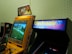 A vintage arcade setup featuring two arcade machines. The first is a yellow Crazy Taxi arcade machine with a steering wheel, featuring vibrant signage at the top displaying 'Crazy Taxi High Roller' with flames. The screen shows a driving game landscape with roads and trees. Next to it is another machine with a sign that reads 'Electronic Experience' with a colorful design, though its screen is not lit.