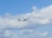 An airplane with branding and logo visible on its side flies amidst a partly cloudy sky, with a few birds soaring nearby. The scene suggests an in-flight journey of the aircraft against a backdrop of fluffy clouds.