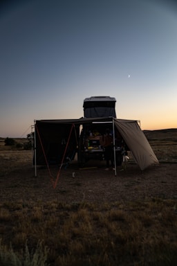 A camper setting up a rooftop tent under a clear blue sky at sunset