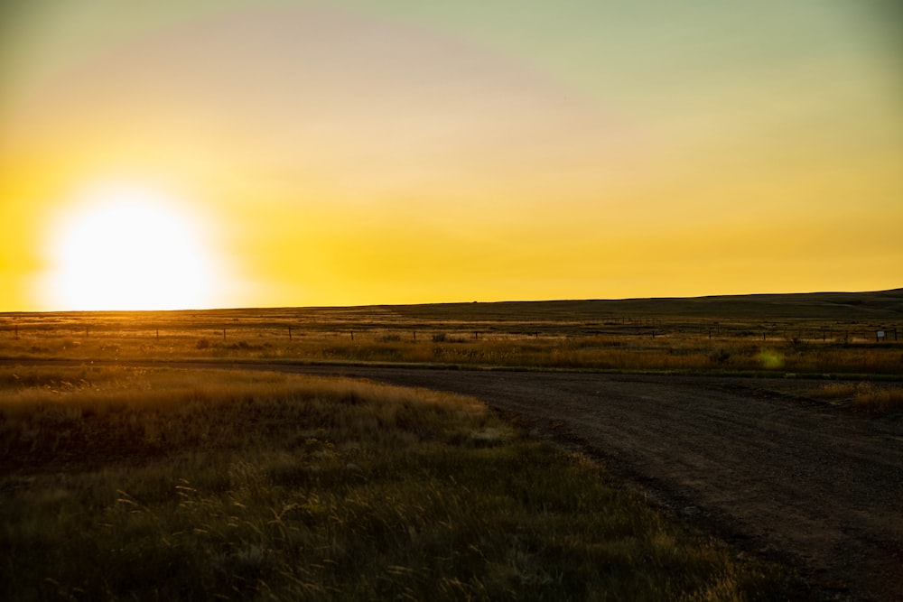 the sun is setting over a dirt road