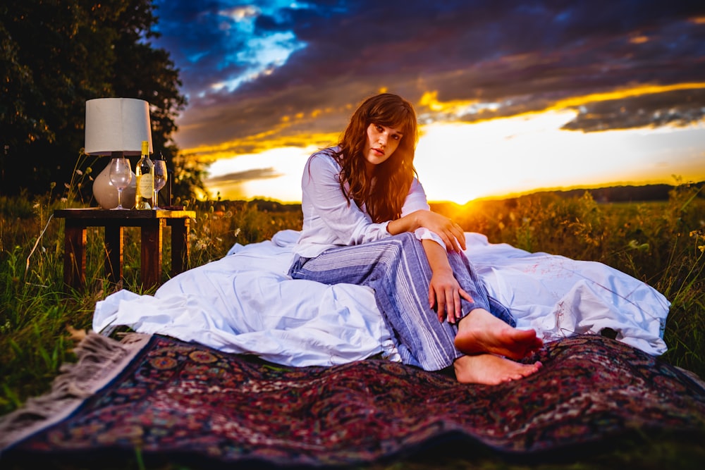 a woman sitting on top of a blanket on top of a field