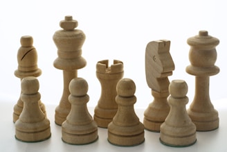 A collection of wooden chess pieces is neatly arranged against a white background. The set includes a king, queen, bishops, knights, rooks, and pawns, all carved in a simple yet elegant design.