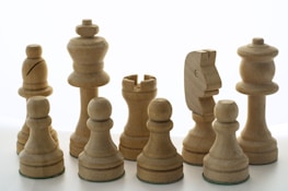 A collection of wooden chess pieces is neatly arranged against a white background. The set includes a king, queen, bishops, knights, rooks, and pawns, all carved in a simple yet elegant design.