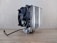 A large cooling fan attached to a metallic heatsink assembly rests on a wooden surface. The design features numerous metal fins and pipes extending down, reflecting light. A black cable is visible, suggesting connectivity for power or electronics.