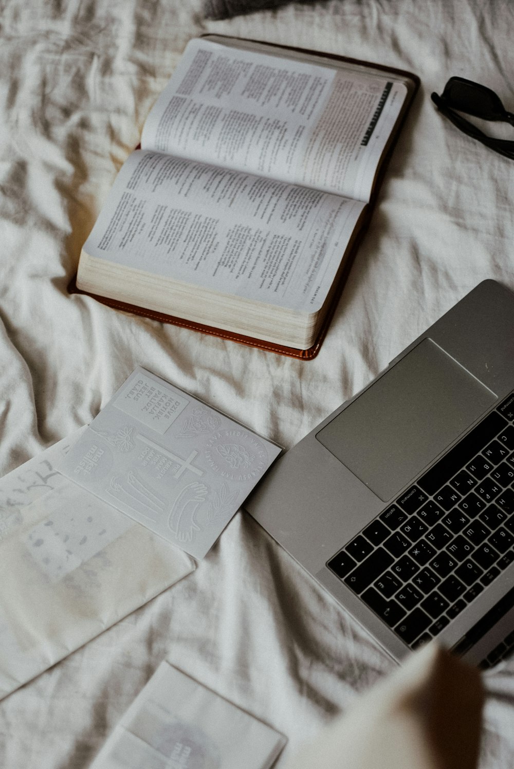 a laptop computer sitting on top of a bed next to an open book