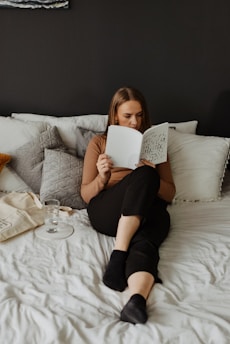 A serene scene of a black woman reading a book surrounded by peaceful, warm lighting and soft pillows.