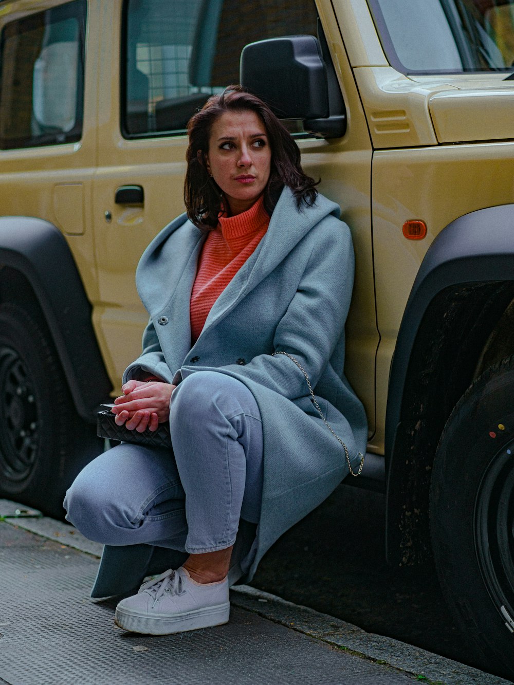 a woman sitting on a curb next to a yellow vehicle