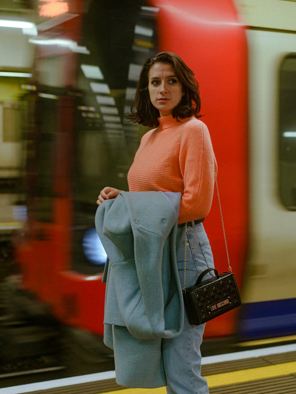 a woman standing on a train platform holding a purse