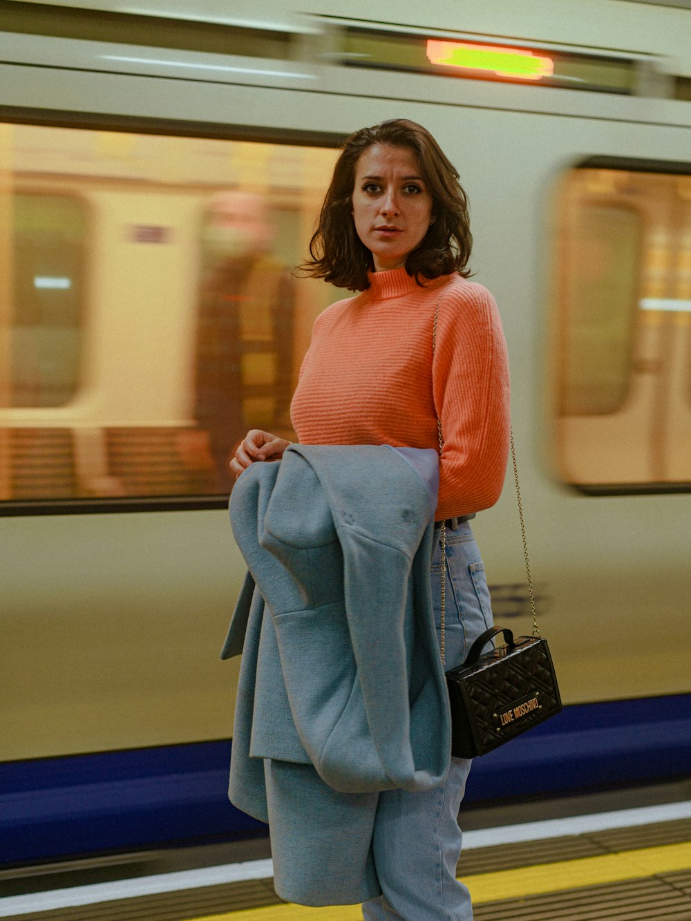a woman standing on a train platform with a purse in her hand