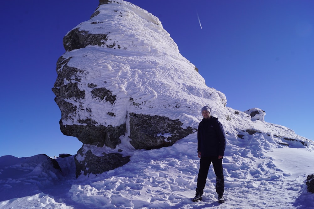 a man standing next to a large rock covered in snow