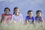 Children playing outside a cabin on a grassy area with mountains in the background.