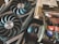 A close-up of a computer graphics card with two large cooling fans labeled ROG Strix, alongside a package of thermal paste labeled Conductonaut and a bottle of liquid cooling solution. The items appear to be for enhancing computer performance and cooling.