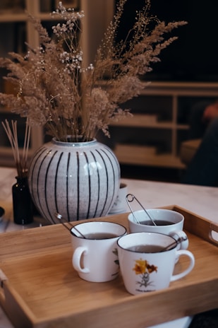 Close-up of delicate tea cups arranged on a light wood tea tray with sunlit tea steam rising.