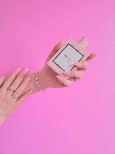 a woman's hand holding a perfume bottle in front of a pink background