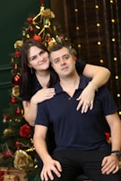 Couple holding hands in front of a large Christmas tree with glowing ornaments