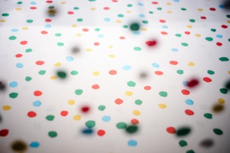 A pattern of variously colored dots scattered across a white background. The dots include red, green, yellow, and blue, arranged in no particular order, creating a playful and vibrant aesthetic.