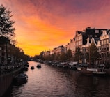 A panoramic view of Amsterdam's canals lined with colorful historic houses at sunset.