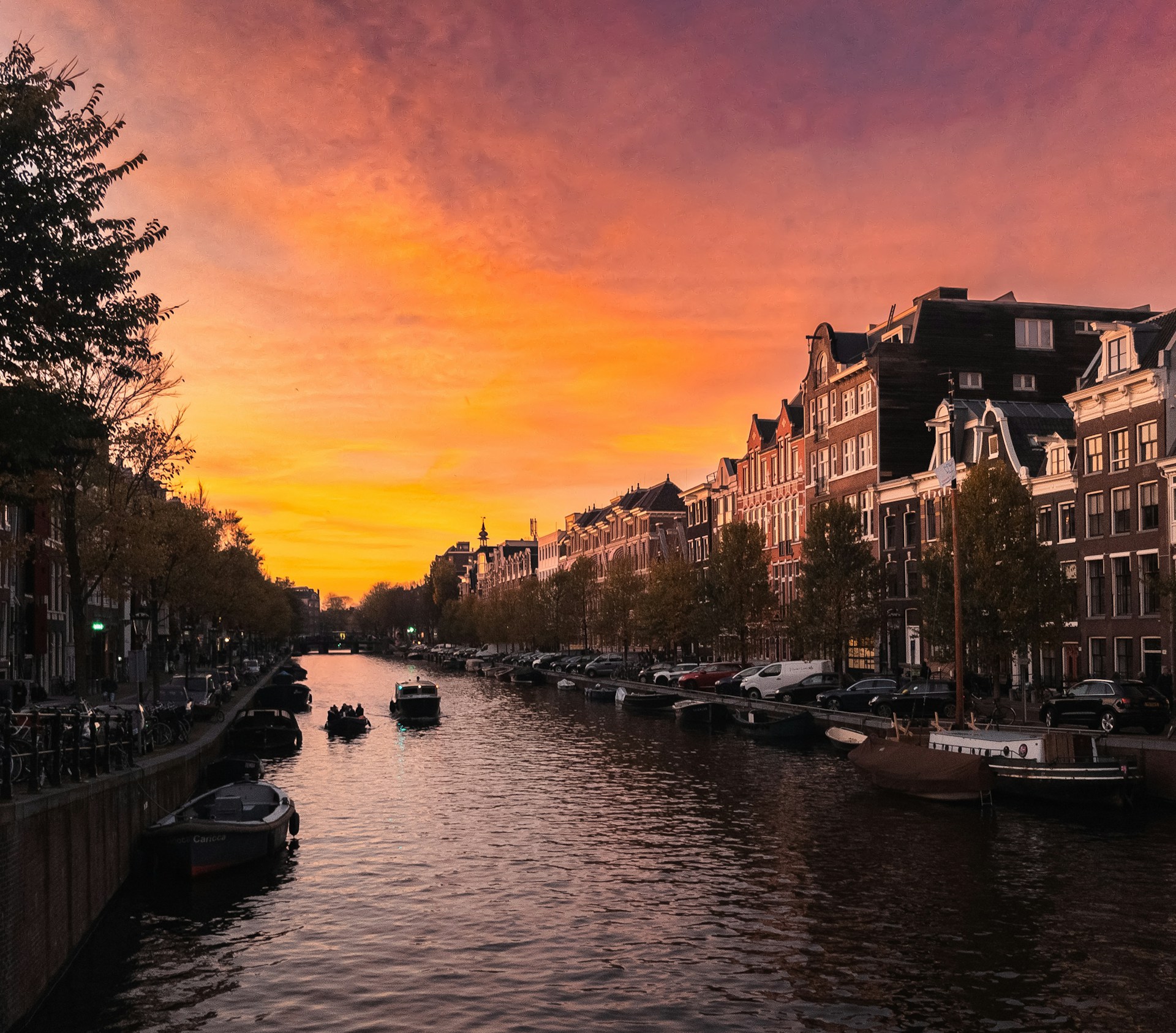 A vibrant sunset over Amsterdam's iconic canals, with historic narrow houses reflecting in the water.