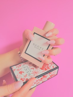 a woman's hand holding a small box with a perfume