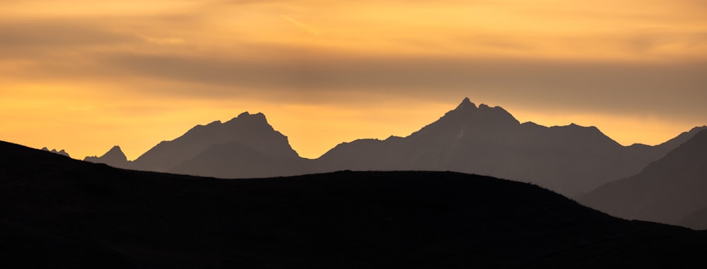 the silhouette of a mountain range against a cloudy sky