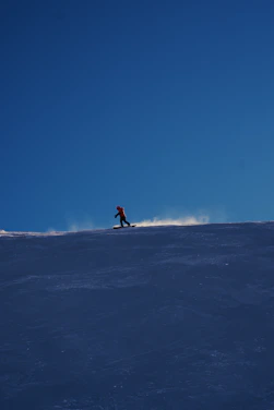 A snowboarder cruising down a snowy hill with a Chug Chariot strapped securely, cans gleaming in the sun.